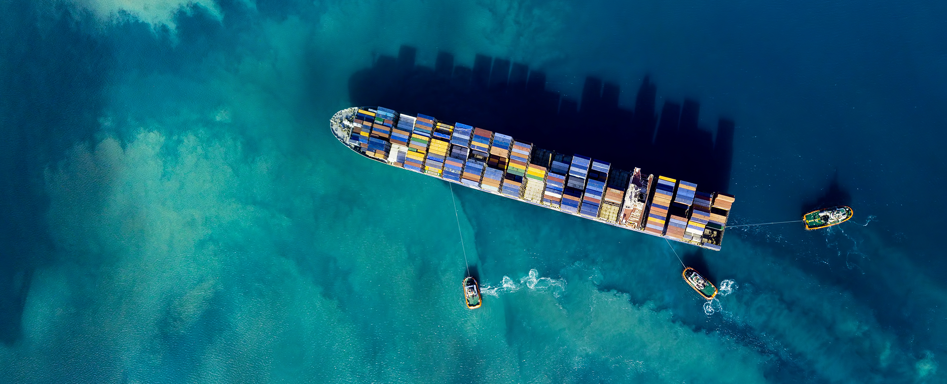 Ariel view of cargo ship over reef, with three small tug boats surrounding it